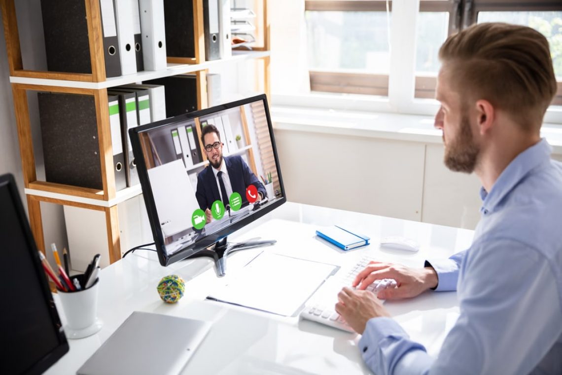 Side view of businessman video conferencing with coworker on desktop PC at office desk